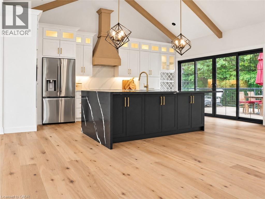 Modern kitchen featuring a black-fronted island with waterfall countertop edge, stainless steel appliances including a French-door refrigerator, and a ceiling-mounted wood hood - 515 Hamilton Drive, Ancaster, ON