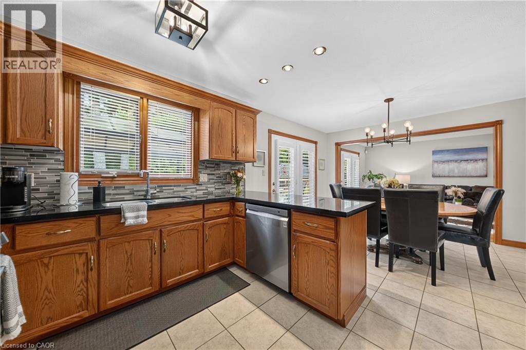 Wood cabinetry with black countertops, tile backsplash, and stainless steel dishwasher - 52 Archwood Crescent, Cambridge, ON