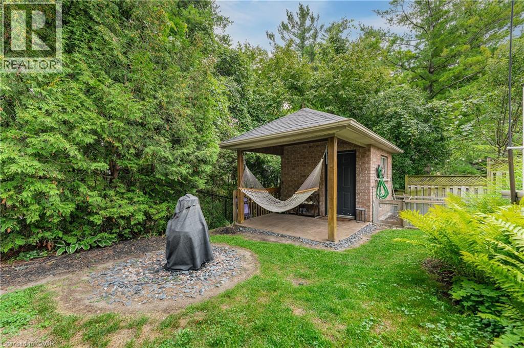 Manicured lawn with mature perimeter landscaping, brick shed with covered patio, and a privacy fence - 52 Archwood Crescent, Cambridge, ON