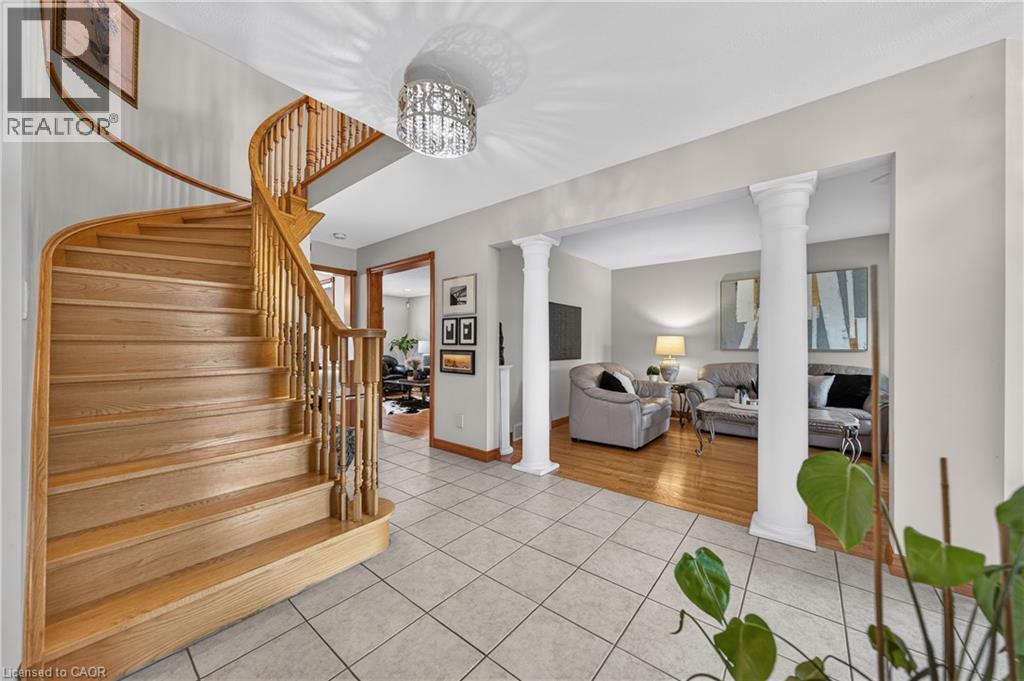Curved wood staircase with traditional balusters, tile flooring, decorative chandelier, and architectural columns - 52 Archwood Crescent, Cambridge, ON