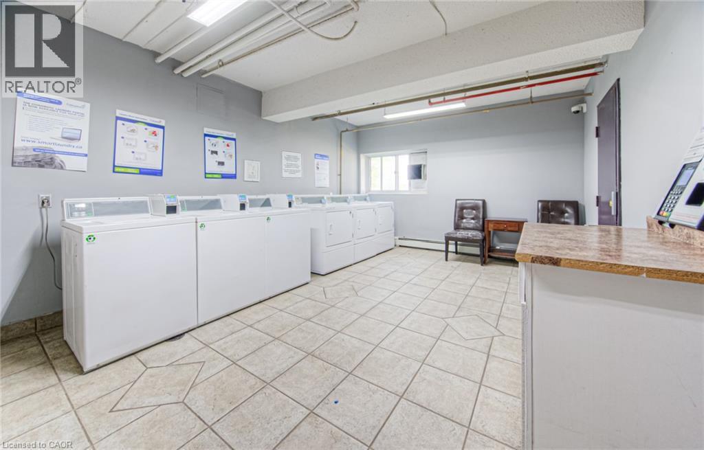 Community laundry room featuring light tile patterned floors, separate washer and dryer, and baseboard heating - 283 Fairway Road N Unit# 501, Kitchener, ON