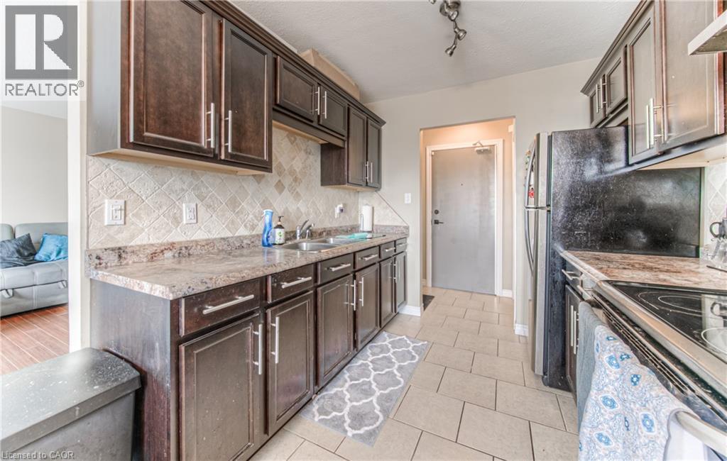 Kitchen featuring tasteful backsplash, dark brown cabinetry, light tile patterned flooring, and under cabinet range hood - 283 Fairway Road N Unit# 501, Kitchener, ON