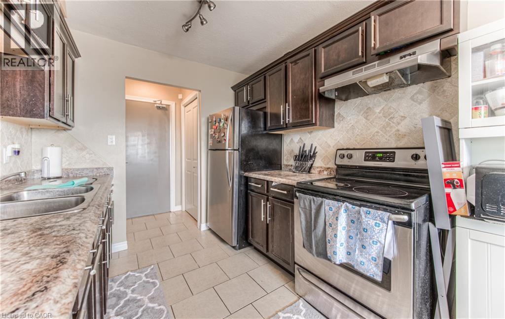 Kitchen with backsplash, appliances with stainless steel finishes, under cabinet range hood, and dark brown cabinetry - 283 Fairway Road N Unit# 501, Kitchener, ON
