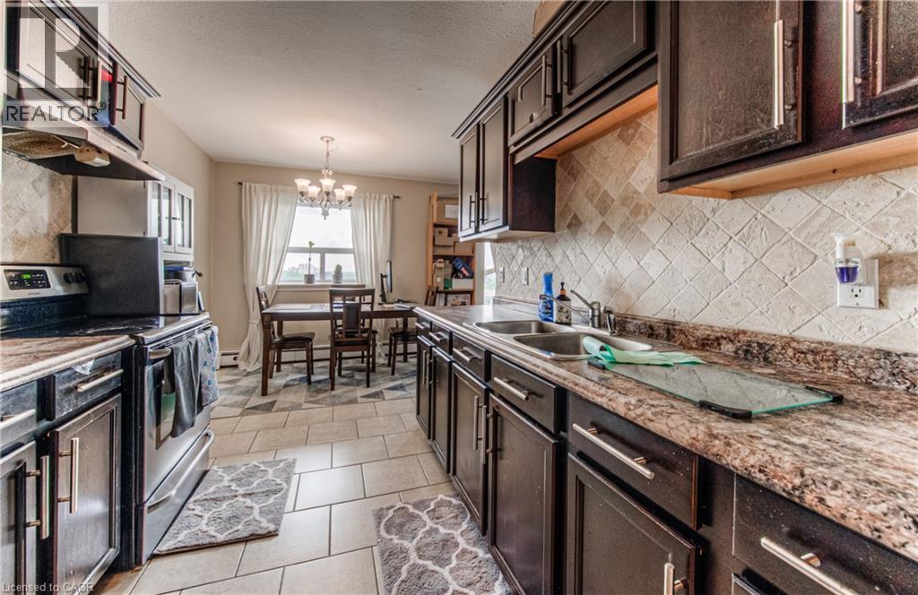 Kitchen featuring stainless steel range with electric stovetop, dark brown cabinets, a chandelier, and a textured ceiling - 283 Fairway Road N Unit# 501, Kitchener, ON