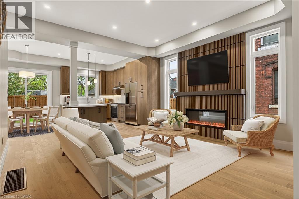 Open-concept living space with wood-finish flooring, a contemporary linear fireplace with slatted wood surround, and recessed lighting - 279 Hess Street S, Hamilton, ON