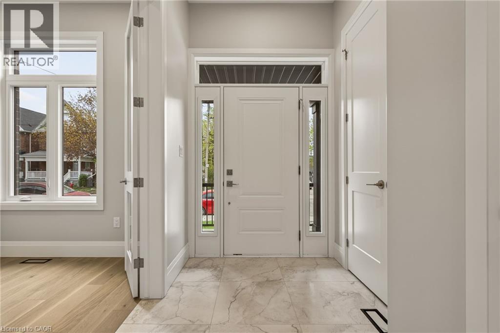 Foyer featuring a paneled entry door with sidelights and transom window, marble-look tile flooring, and wood-finish flooring - 279 Hess Street S, Hamilton, ON