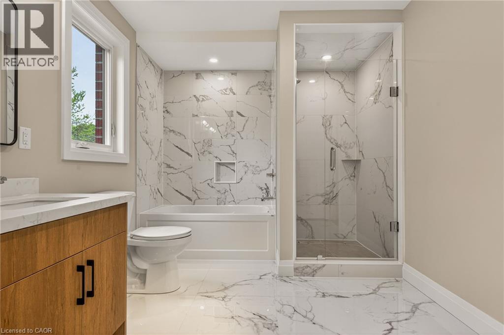 Bathroom featuring a glass-enclosed shower, a built-in tub with wall tile surround, a single vanity with a light wood-finish cabinet, a white countertop, and white tile flooring - 279 Hess Street S, Hamilton, ON