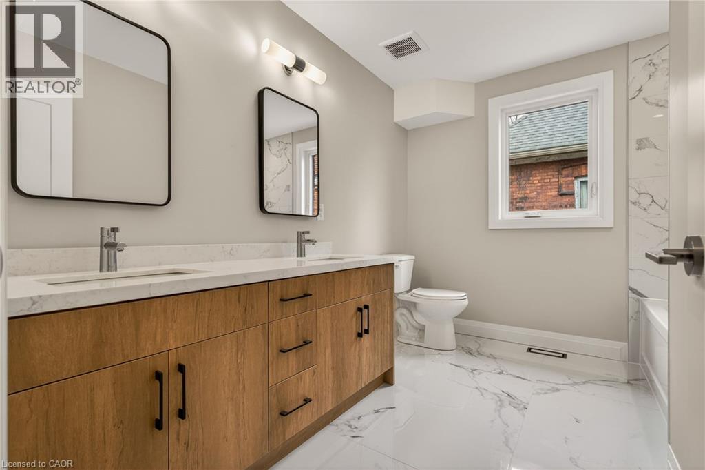 Dual sink vanity with wood-finish cabinetry, white countertop, and contemporary black-framed mirrors - 279 Hess Street S, Hamilton, ON