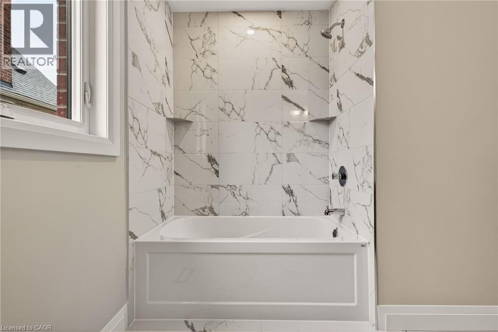 Bathtub with surround of marble-look tile, integrated shelving, and a dark-finish shower head and faucet - 279 Hess Street S, Hamilton, ON
