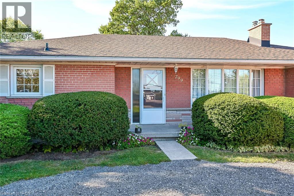 Brick facade residence with a pitched roof, featuring a concrete entry and mature shrubbery - 799 Highway 6, Caledonia, ON