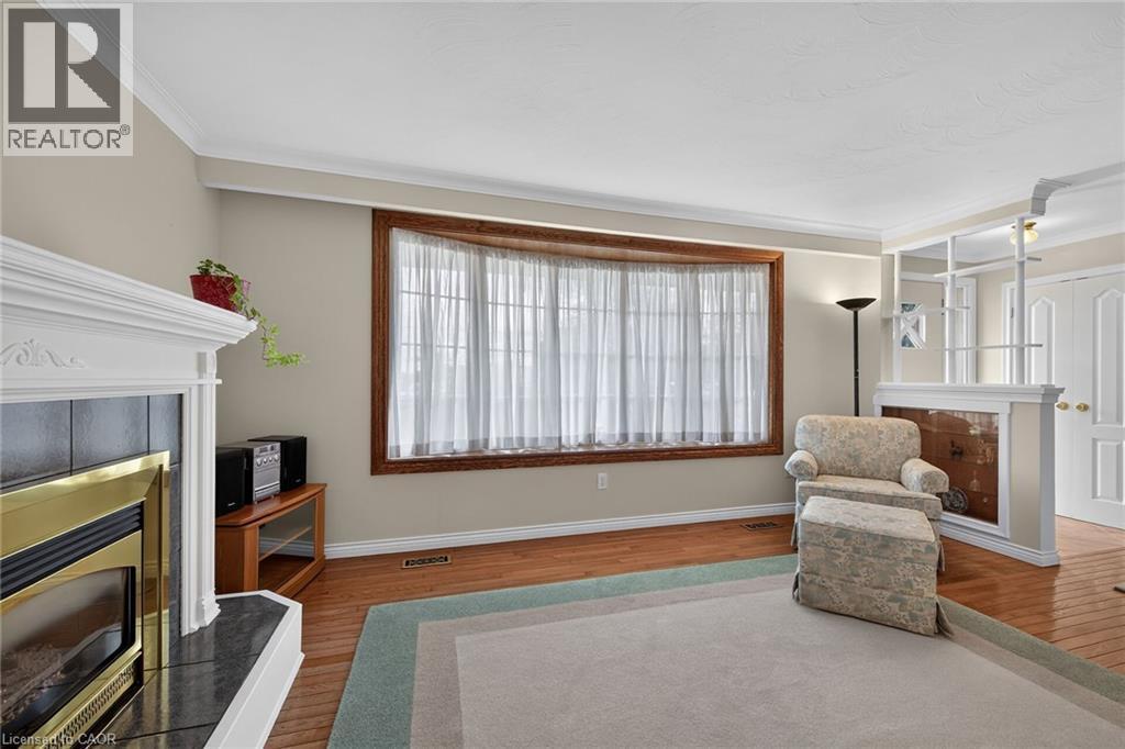 Wood-finish flooring, white crown molding, bay window with wood trim, white fireplace with dark hearth, and a built-in room divider - 799 Highway 6, Caledonia, ON