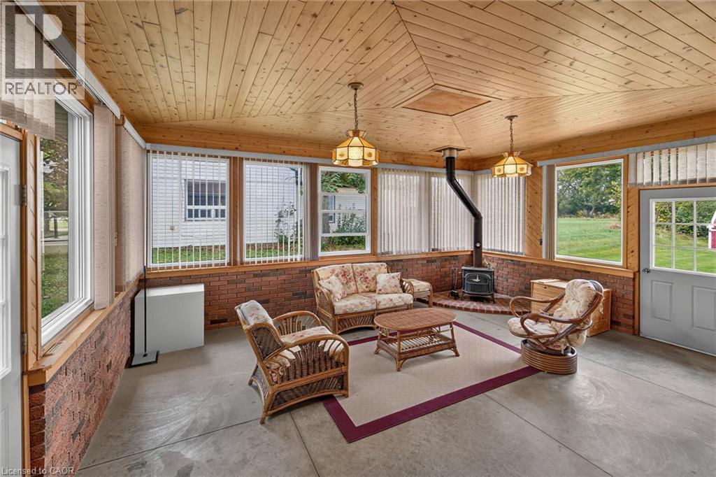 Wood-paneled ceiling, brick-finish wall accents, multiple windows, built-in wood-burning stove, and a light-colored entry door - 799 Highway 6, Caledonia, ON