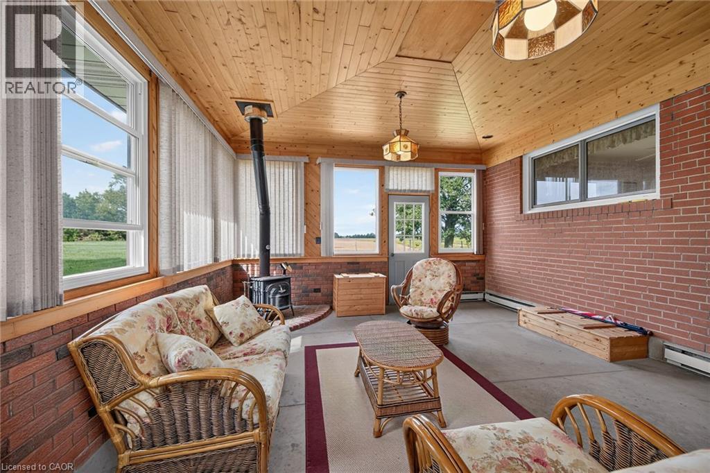 Sunroom featuring a wood-paneled vaulted ceiling, exposed brick walls, and a freestanding wood-burning stove - 799 Highway 6, Caledonia, ON
