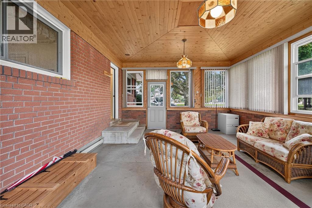 Enclosed sunroom featuring a vaulted wood-paneled ceiling, brick wall, multiple windows with vertical blinds, and a concrete floor - 799 Highway 6, Caledonia, ON