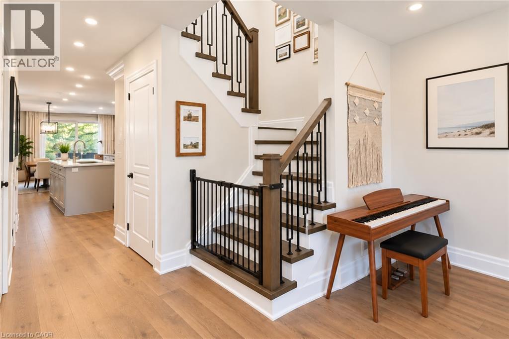 Light wood-finish flooring extending through the entry, staircase with dark wood-finish handrail and black metal balusters, recessed lighting, and white baseboards - 2409 Postmaster Drive, Oakville, ON