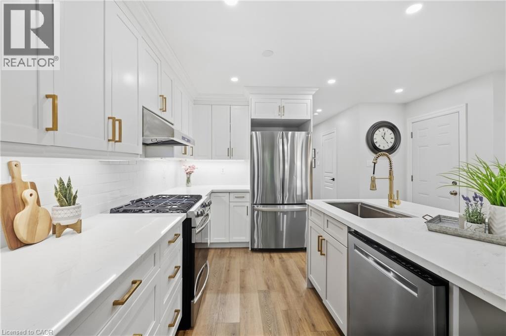 White cabinetry with gold-tone hardware, stainless steel appliances, wood-finish flooring, recessed lighting, and a kitchen island with an undermount sink - 2409 Postmaster Drive, Oakville, ON