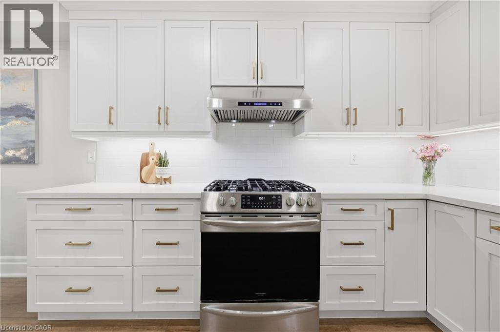 White shaker cabinetry with gold-tone hardware, stainless steel gas range, coordinating range hood, white subway tile backsplash, and light-toned countertops - 2409 Postmaster Drive, Oakville, ON