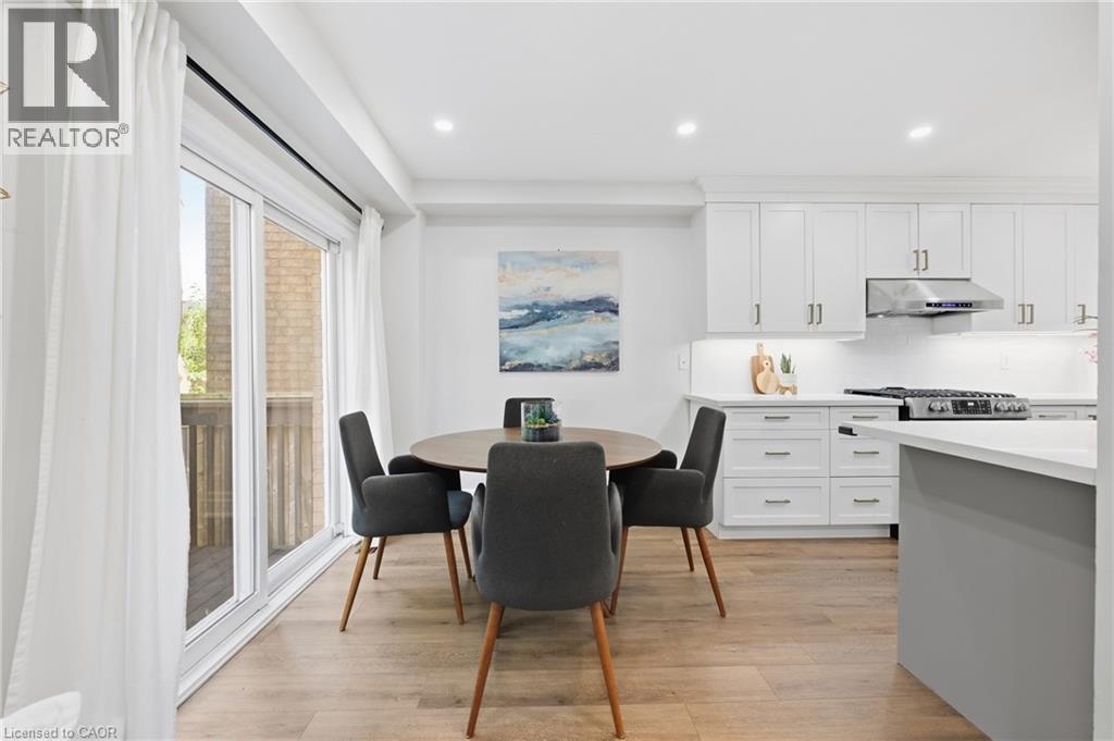 Kitchen and dining area featuring wood-finish flooring, white cabinetry with silver-tone hardware, a stainless steel range and range hood, and recessed lighting - 2409 Postmaster Drive, Oakville, ON