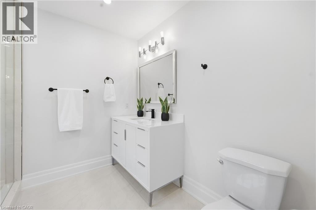 White vanity with integrated sink, matte black faucet, wall-mounted lighting fixture, framed mirror, and glass shower enclosure - 2409 Postmaster Drive, Oakville, ON