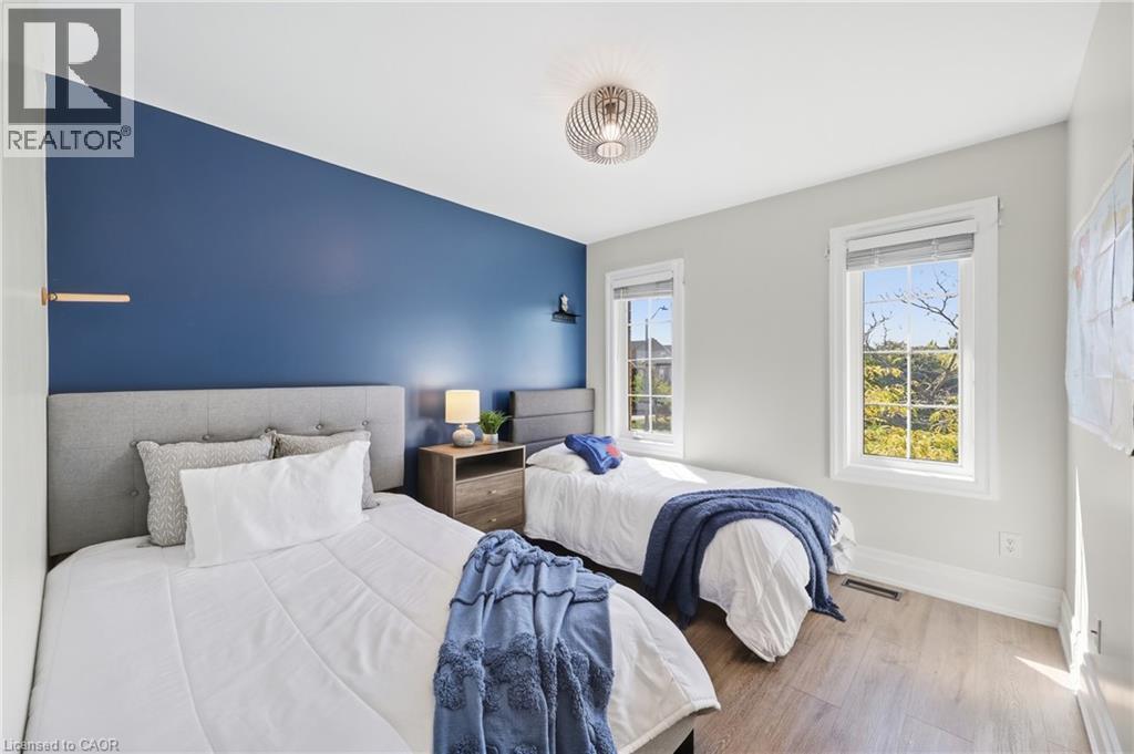 Room featuring wood-finish flooring, two large windows, a textured accent wall, and a contemporary ceiling light fixture - 2409 Postmaster Drive, Oakville, ON