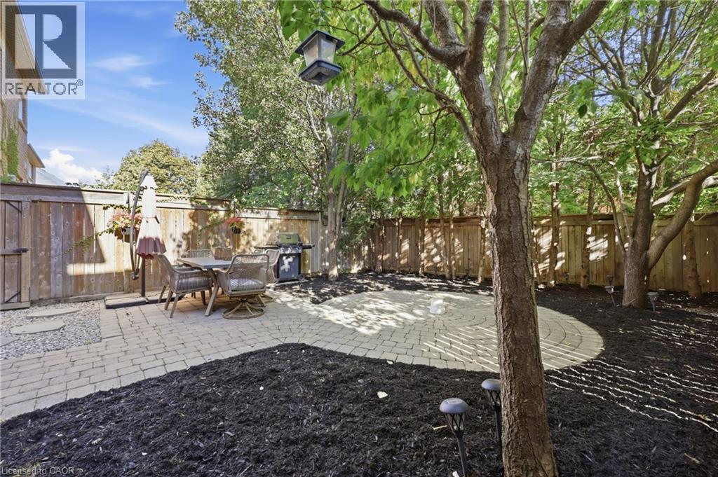 Backyard featuring a circular paver patio, wood fencing, and established trees - 2409 Postmaster Drive, Oakville, ON