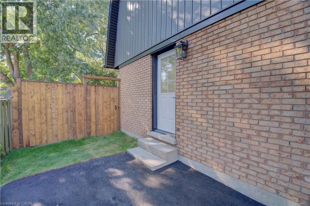 Brick exterior featuring a white entry door with glass panels, exterior lighting, and concrete steps - 210 Ferguson Avenue, Cambridge, ON