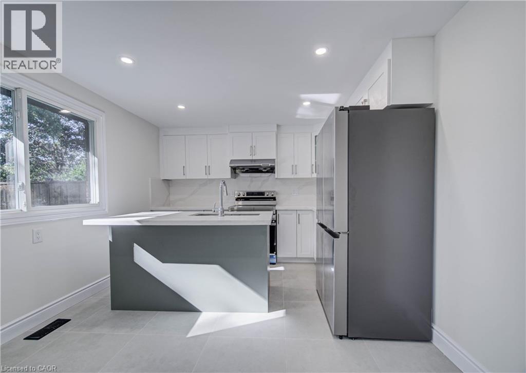 Kitchen featuring an island with a light-toned countertop, white cabinetry, a stainless steel refrigerator, and tiled flooring - 210 Ferguson Avenue, Cambridge, ON
