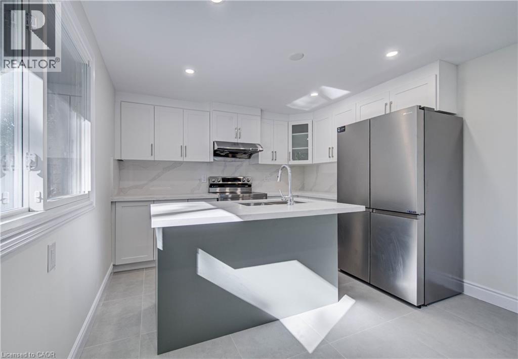White shaker cabinetry, stainless steel appliances, central island with sink, recessed ceiling lighting, and light-toned flooring - 210 Ferguson Avenue, Cambridge, ON