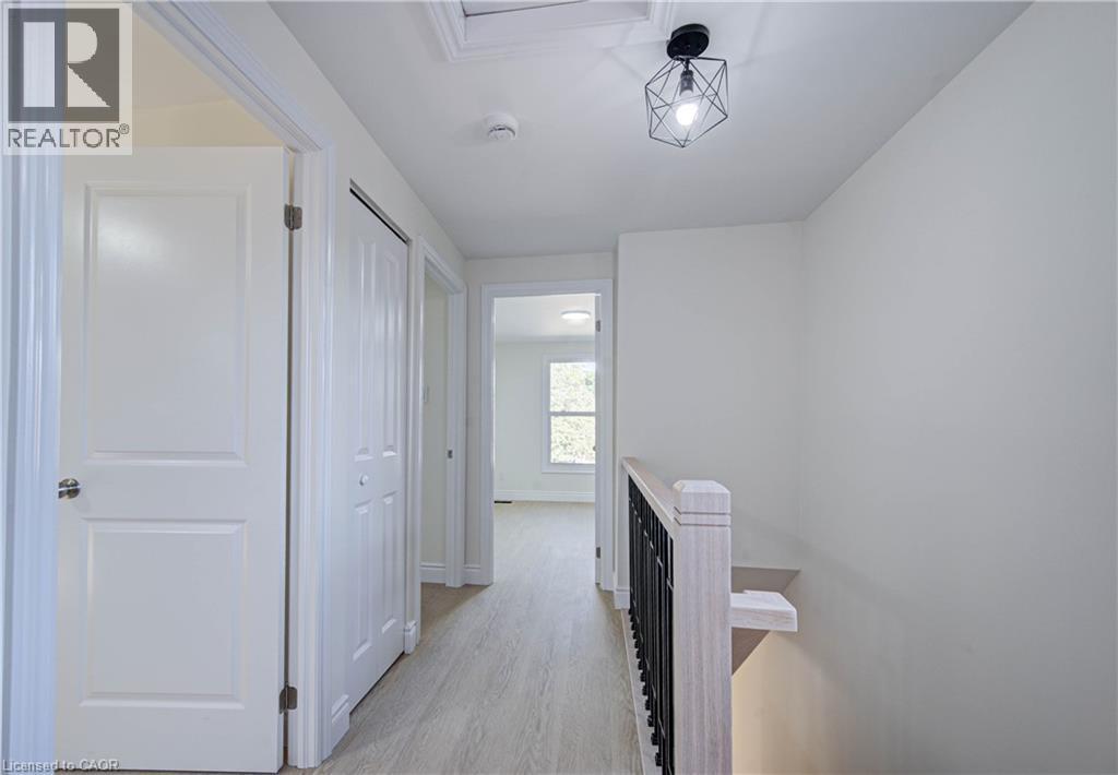Hallway featuring wood-finish flooring, white paneled doors, a geometric light fixture, and a wood and metal railing - 210 Ferguson Avenue, Cambridge, ON