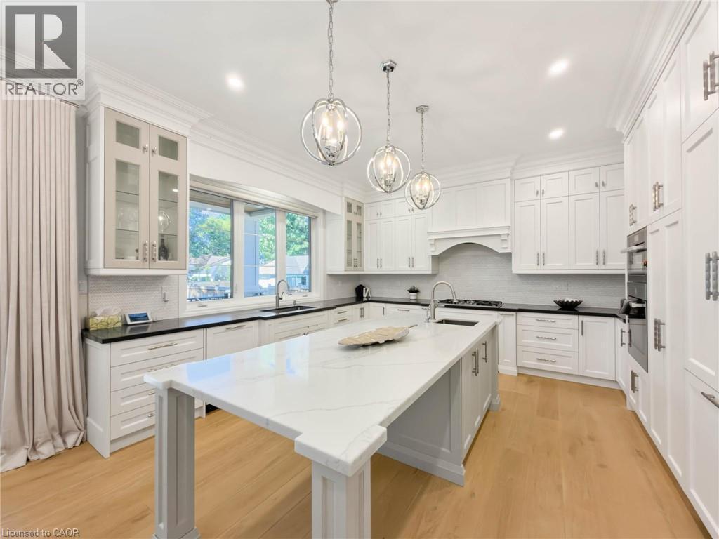 Gourmet kitchen featuring a large central island with light-toned countertops, extensive white cabinetry, wood-finish flooring, recessed lighting, and modern pendant fixtures - 236 Poplar Drive, Burlington, ON
