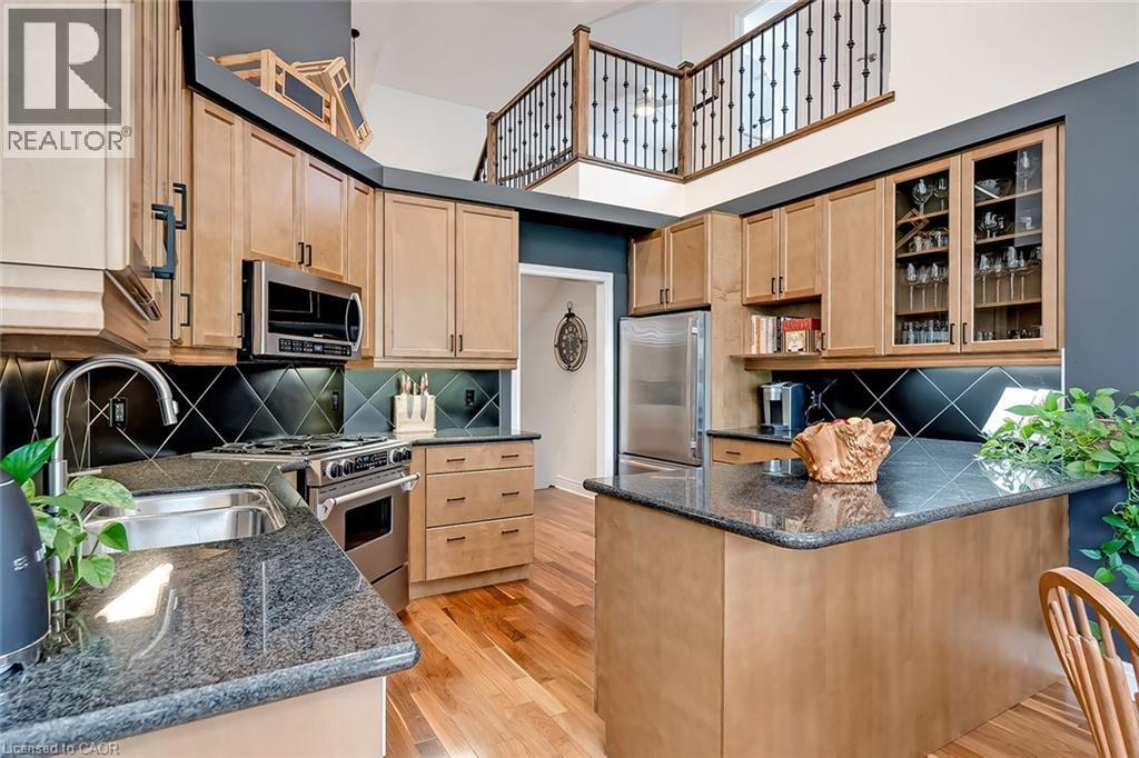 Kitchen featuring wood-finish cabinetry, stainless steel appliances, dark granite countertops, and a black tile backsplash - 4285 Couples Crescent, Burlington, ON
