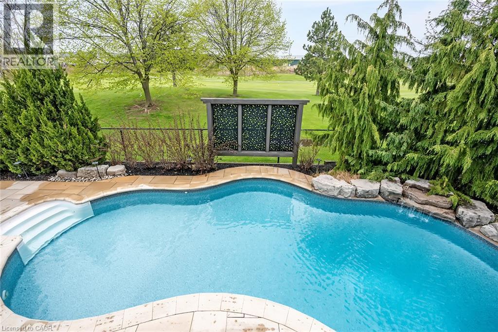 Curved swimming pool with integrated steps, surrounded by stone coping and mature landscaping - 4285 Couples Crescent, Burlington, ON