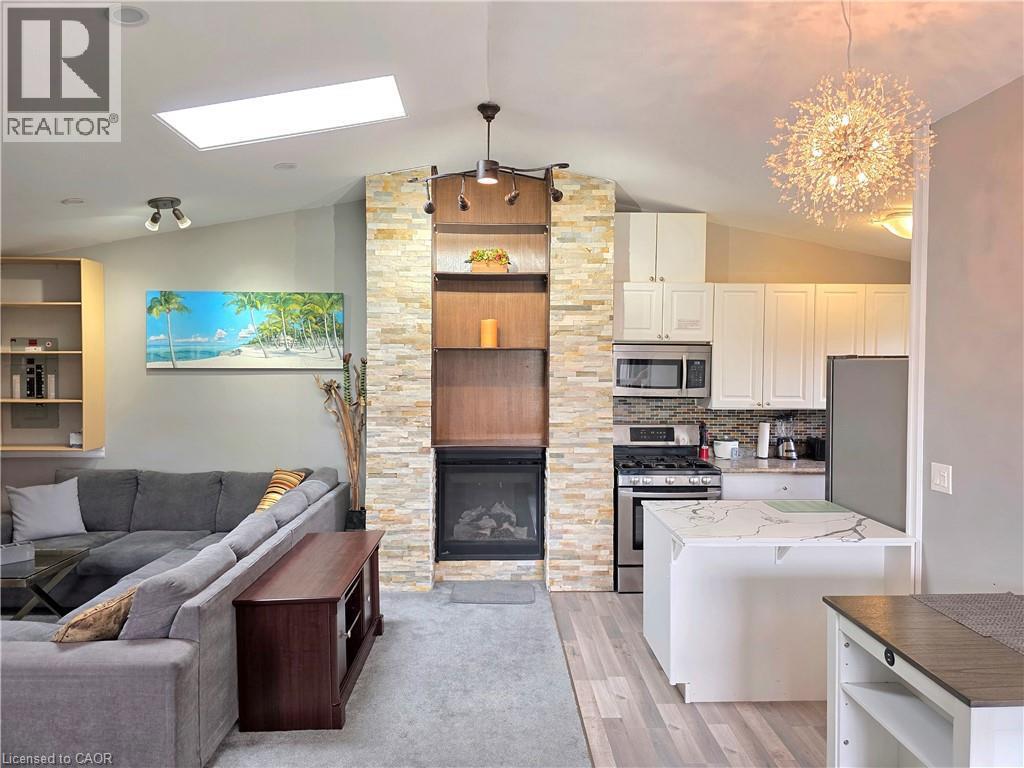 Open-concept living space featuring a stacked stone fireplace with built-in shelving, vaulted ceilings, and a skylight - 16 Forest Hill Road, St. Catharines, ON