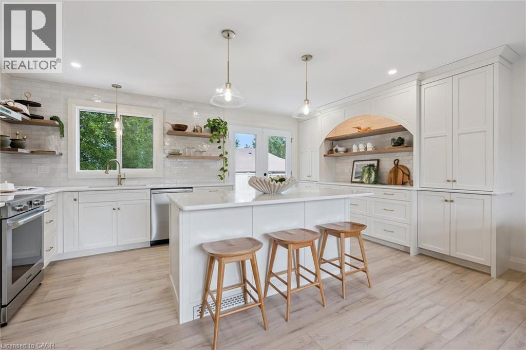Kitchen featuring white cabinetry, wood-finish flooring, a central island with countertop, stainless steel appliances, and open shelving - 8 Christian Street, Baden, ON
