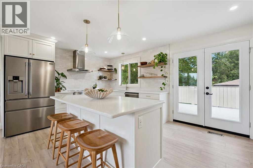 Kitchen featuring a center island with a light-toned countertop, stainless steel appliances, a tile backsplash, wood-finish flooring, and double glass-paned doors - 8 Christian Street, Baden, ON