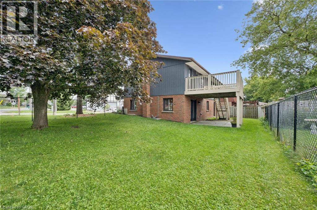 Expansive green space featuring mature trees, a multi-level wood deck, a chain-link fence, and a brick and siding exterior - 8 Christian Street, Baden, ON