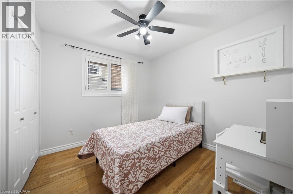 Comfortable bedroom featuring wood-finish flooring, a ceiling fan with integrated lighting, and ample natural light from a window with plantation shutters - 6346 Neuchatel Road, Mississauga, ON
