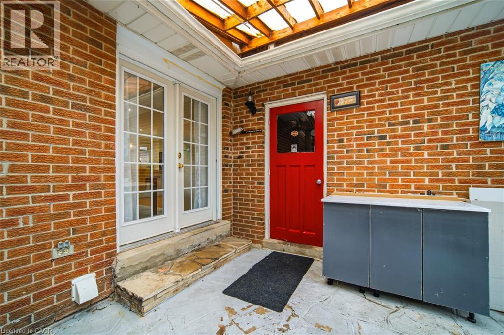 Brick exterior patio featuring a red entry door, white French doors, and an overhead pergola - 6346 Neuchatel Road, Mississauga, ON