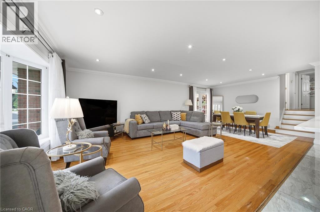 Spacious living area featuring hardwood flooring throughout, recessed ceiling lighting, and multiple seating zones anchored by a gray upholstered sectional sofa - 6346 Neuchatel Road, Mississauga, ON