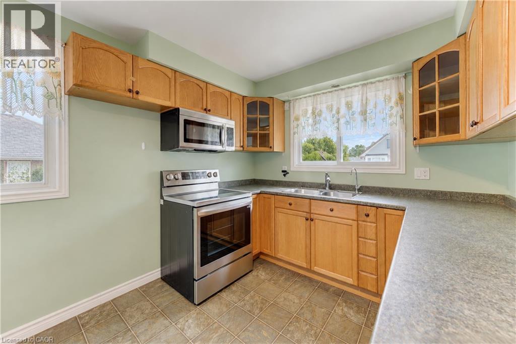 Kitchen featuring wood cabinetry, stainless steel appliances, a double basin sink, and tile flooring - 64 Stanley Street, Cambridge, ON