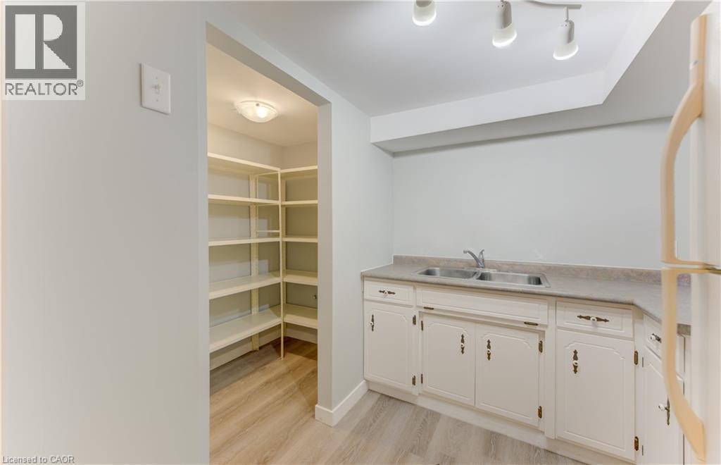 Galley kitchen featuring white cabinetry, a double basin stainless steel sink, and wood-finish flooring - 64 Stanley Street, Cambridge, ON