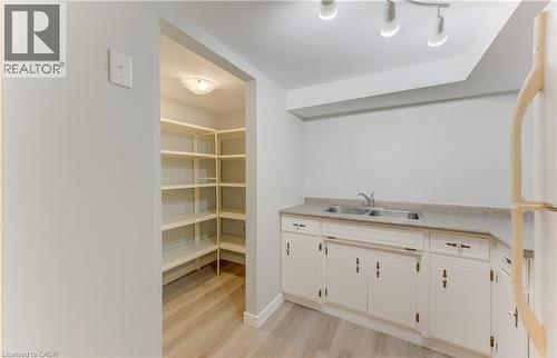 Galley kitchen featuring white cabinetry, a double basin stainless steel sink, and wood-finish flooring - 64 Stanley Street, Cambridge, ON 