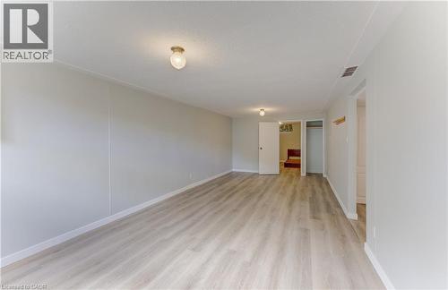 Spacious room featuring wood-finish flooring, light neutral wall paint, and ceiling-mounted light fixtures - 64 Stanley Street, Cambridge, ON 