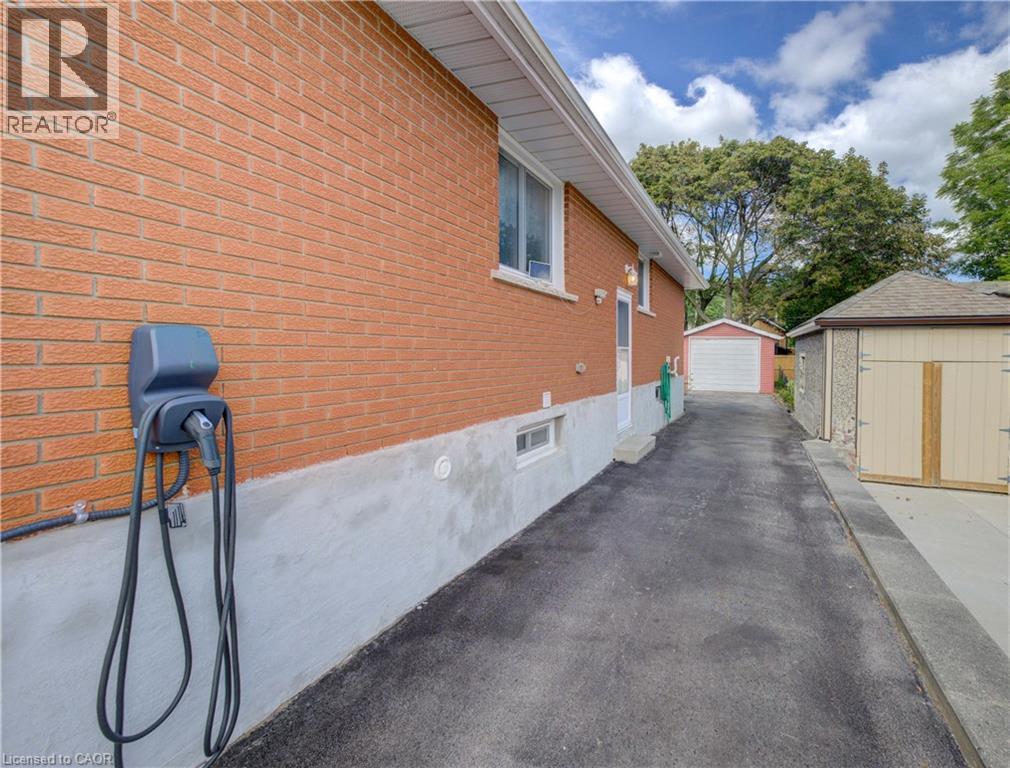 Brick exterior with EV charging station, asphalt driveway, detached garage, and additional storage shed - 64 Stanley Street, Cambridge, ON