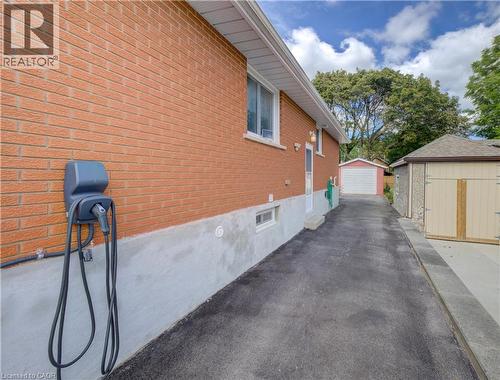 Brick exterior with EV charging station, asphalt driveway, detached garage, and additional storage shed - 64 Stanley Street, Cambridge, ON 