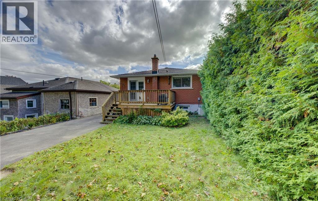 Rear exterior with brick facade, wood deck, and built-in privacy hedge - 64 Stanley Street, Cambridge, ON
