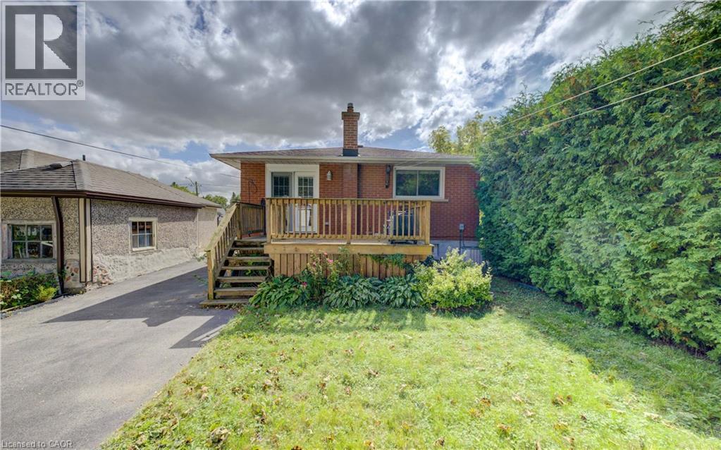 Rear exterior with brick facade, wood deck, and an expansive lawn - 64 Stanley Street, Cambridge, ON