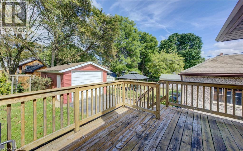 Expansive outdoor deck with wood railing, detached garage with red siding, and a paved driveway - 64 Stanley Street, Cambridge, ON