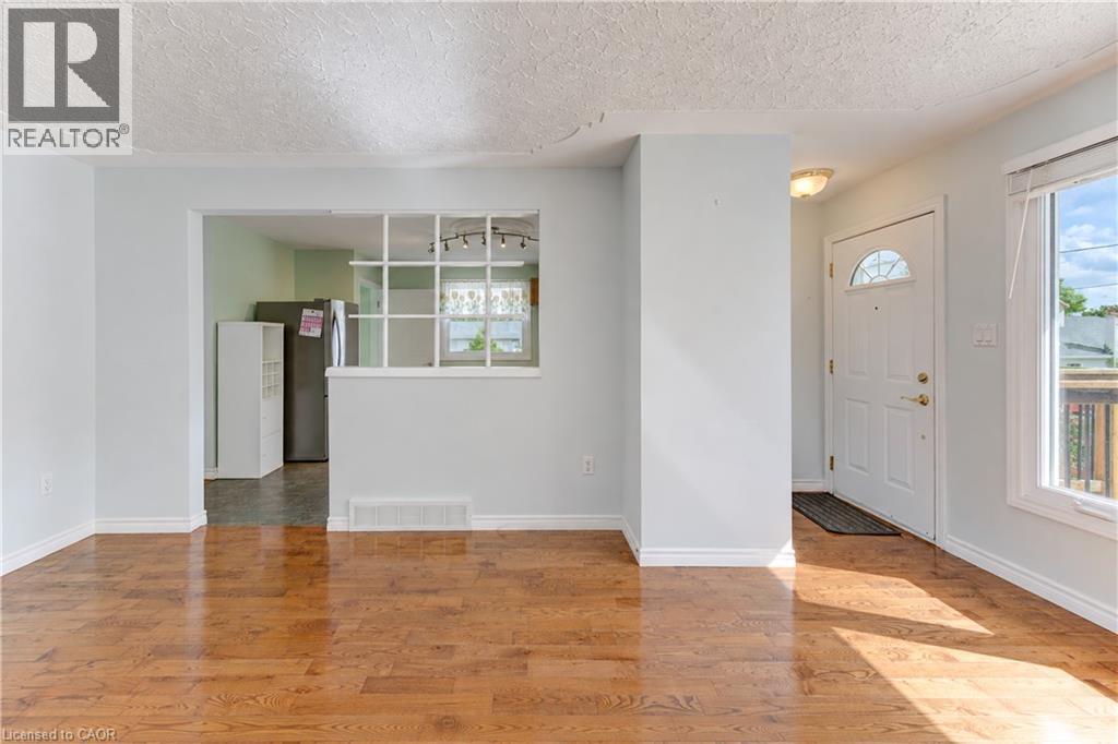 Hardwood-finish flooring, white trim, white front door with arched window, and a partial wall with decorative grid - 64 Stanley Street, Cambridge, ON
