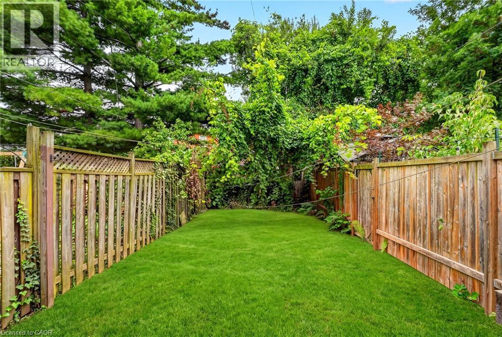 Expansive backyard featuring a manicured lawn, established wooden fencing, and mature perimeter foliage - 199 N Locke Street N, Hamilton, ON
